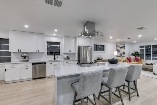 10606 Estate Ln, Dallas, TX 75238 - kitchen featuring stainless steel appliances, a sink, island range hood, a kitchen bar, and light wood-style flooring