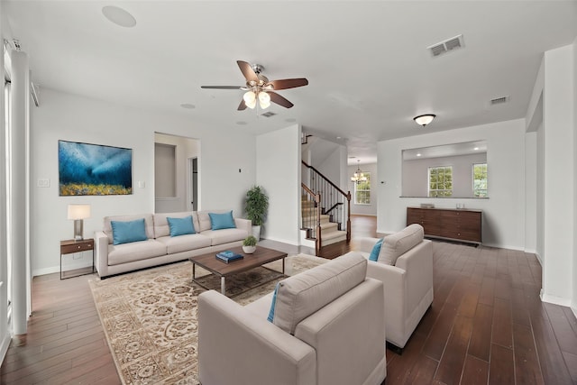 living area with visible vents, baseboards, stairway, dark wood finished floors, and ceiling fan with notable chandelier