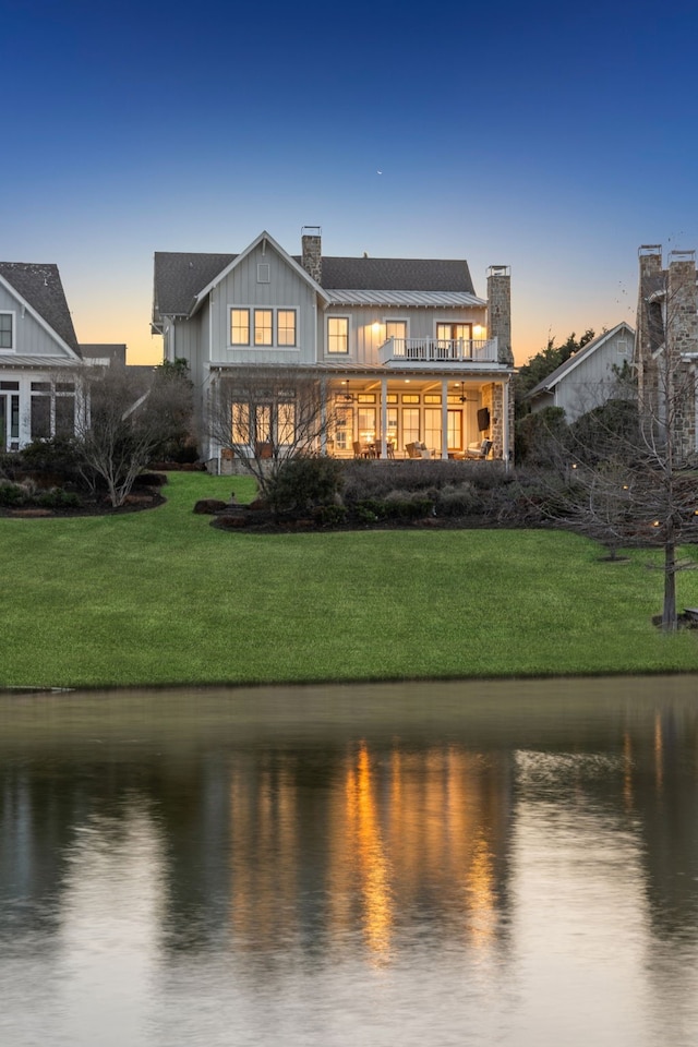 13270 Waterside Dr, Malakoff, TX 75148 - back of house at dusk featuring board and batten siding, a water view, a chimney, and a lawn