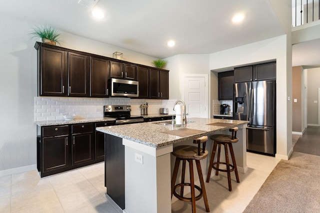 kitchen featuring light stone counters, a sink, stainless steel appliances, decorative backsplash, and a kitchen bar