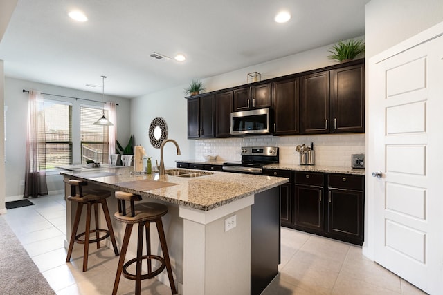 kitchen with light stone counters, a sink, stainless steel appliances, decorative backsplash, and visible vents