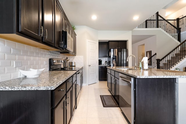 kitchen featuring dark brown cabinetry, tasteful backsplash, a sink, light tile patterned floors, and stainless steel appliances