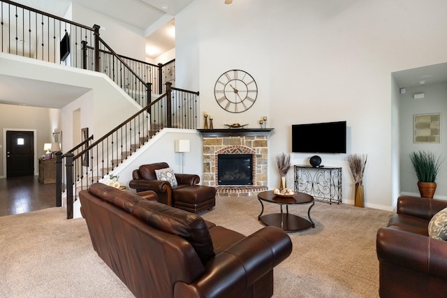 living room with a high ceiling, carpet floors, a stone fireplace, baseboards, and stairway