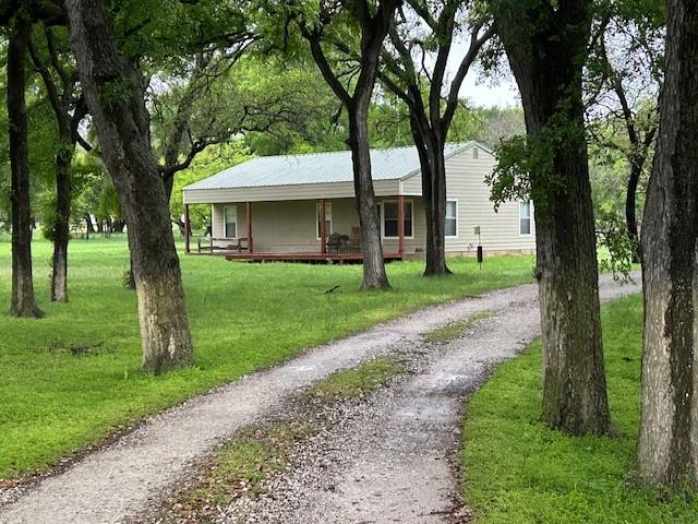 view of front facade featuring covered porch, gravel driveway, and a front lawn