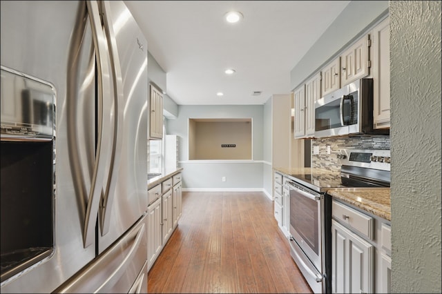 kitchen featuring light stone counters, tasteful backsplash, hardwood / wood-style floors, appliances with stainless steel finishes, and recessed lighting