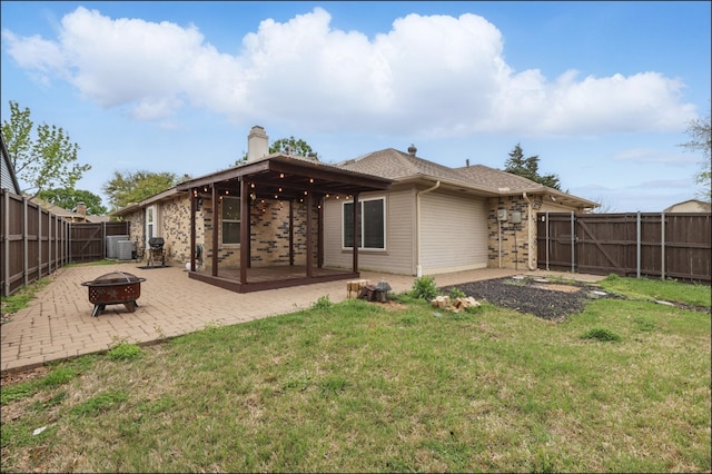 back of house featuring a lawn, a patio area, an outdoor fire pit, and a fenced backyard