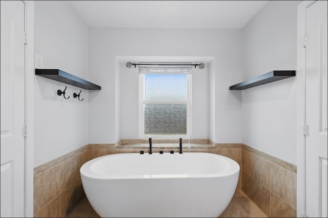 full bathroom featuring a soaking tub, a wainscoted wall, and tile walls