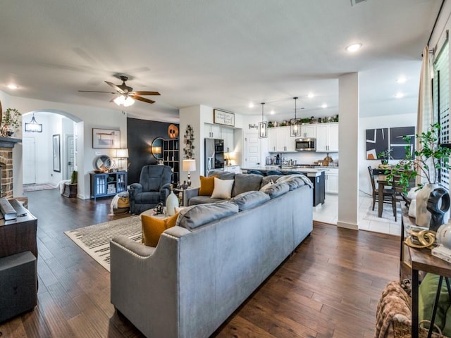 living room with a ceiling fan, arched walkways, dark wood finished floors, baseboards, and recessed lighting