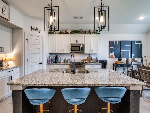 kitchen featuring a kitchen breakfast bar, a sink, stainless steel microwave, visible vents, and backsplash