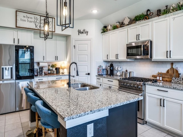 kitchen with a sink, an island with sink, light tile patterned floors, backsplash, and appliances with stainless steel finishes