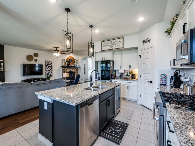 kitchen featuring stainless steel appliances, light tile patterned floors, a sink, a fireplace, and white cabinetry