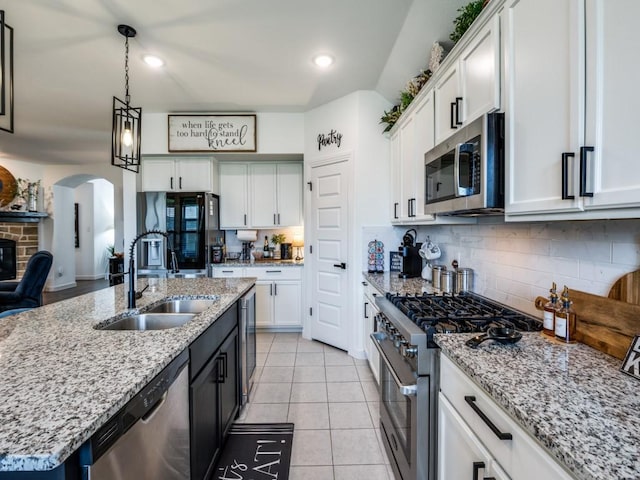 kitchen featuring a sink, decorative backsplash, arched walkways, stainless steel appliances, and white cabinets