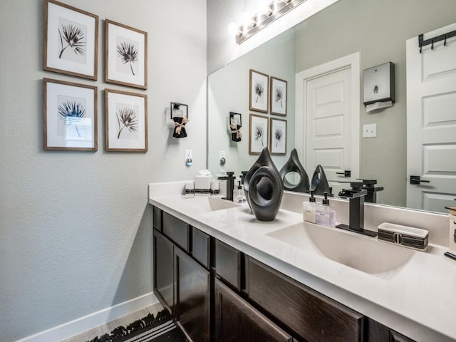 bathroom featuring baseboards, a textured wall, a sink, and double vanity