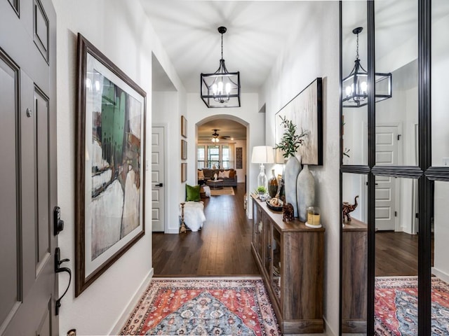entrance foyer with arched walkways, baseboards, wood finished floors, and an inviting chandelier