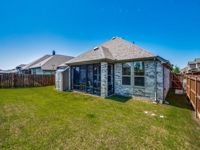 back of house featuring a lawn, a fenced backyard, brick siding, a sunroom, and a storage unit