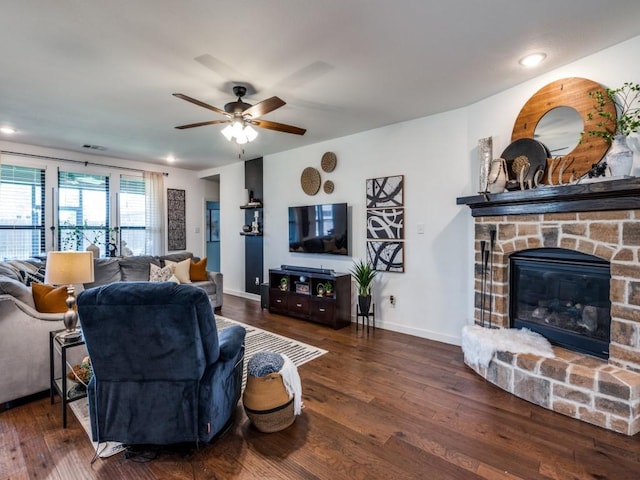 living area featuring a stone fireplace, hardwood / wood-style flooring, ceiling fan, baseboards, and visible vents