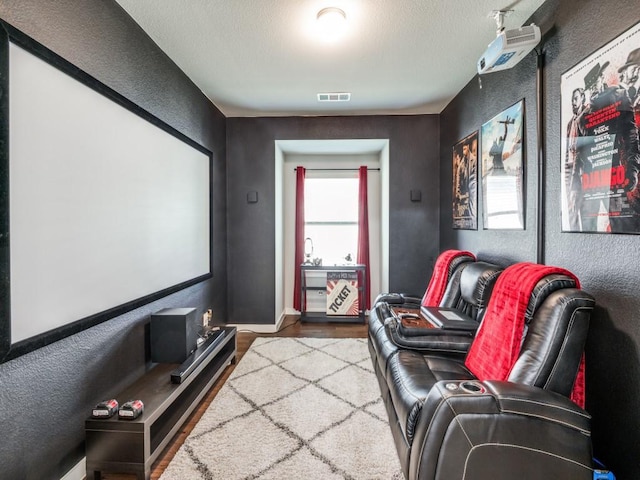 cinema featuring baseboards, a textured wall, wood finished floors, and visible vents