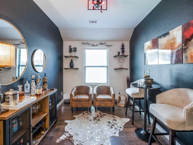 sitting room featuring a textured wall, vaulted ceiling, and visible vents
