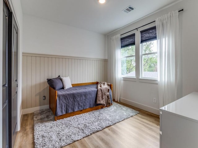 bedroom featuring baseboards, visible vents, wood finished floors, and wainscoting