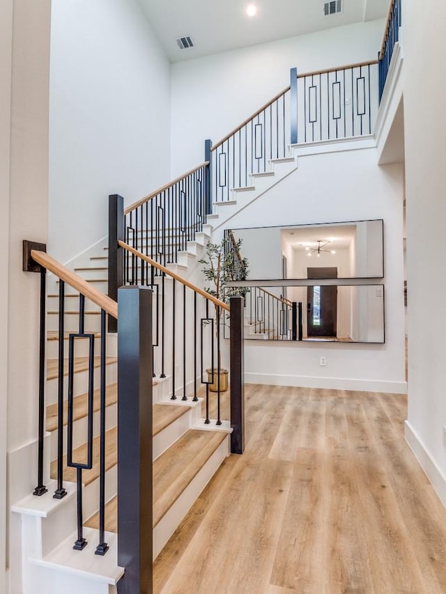 staircase with baseboards, visible vents, a high ceiling, and wood finished floors