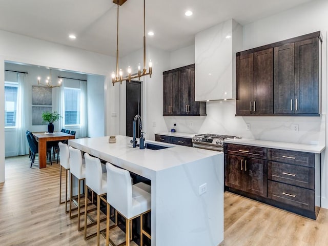 kitchen with a kitchen breakfast bar, an inviting chandelier, a sink, wall chimney range hood, and a kitchen island with sink