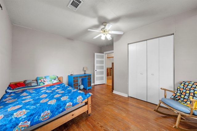 bedroom with a closet, wood finished floors, baseboards, visible vents, and ceiling fan