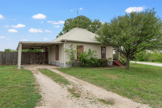 view of side of home featuring metal roof, fence, dirt driveway, an attached carport, and a lawn