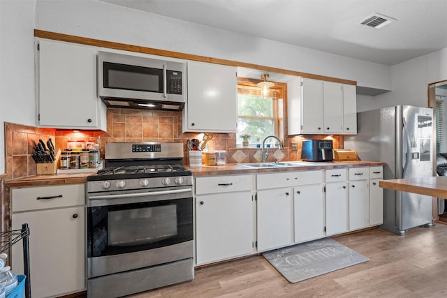 kitchen featuring white cabinetry, stainless steel appliances, a sink, visible vents, and light wood-style flooring