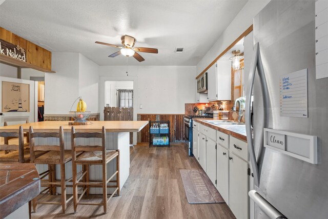 kitchen with a wainscoted wall, a sink, stainless steel appliances, visible vents, and ceiling fan