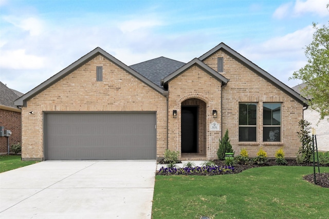 french country inspired facade featuring a front lawn, brick siding, a shingled roof, concrete driveway, and an attached garage