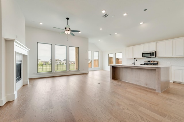 kitchen with a center island with sink, stove, stainless steel microwave, lofted ceiling, and open floor plan