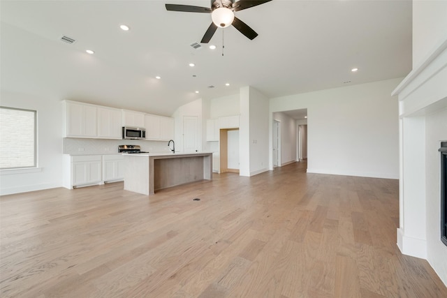 kitchen featuring open floor plan, white cabinetry, a sink, vaulted ceiling, and stainless steel appliances
