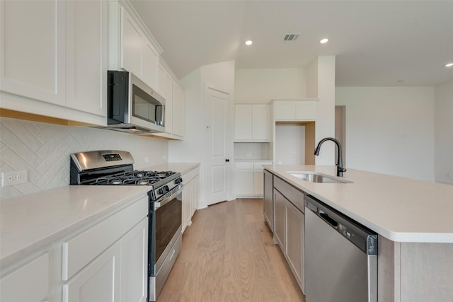 kitchen with visible vents, a sink, light wood finished floors, backsplash, and stainless steel appliances