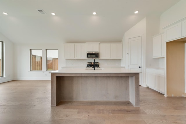 kitchen with visible vents, appliances with stainless steel finishes, tasteful backsplash, vaulted ceiling, and a center island with sink