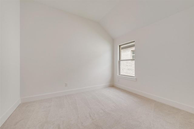spare room featuring baseboards, lofted ceiling, and light carpet