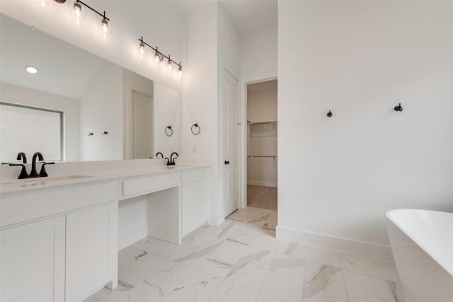 bathroom with double vanity, a walk in closet, a freestanding bath, a sink, and baseboards