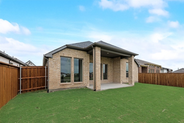 back of property featuring a yard, brick siding, a fenced backyard, and a patio area
