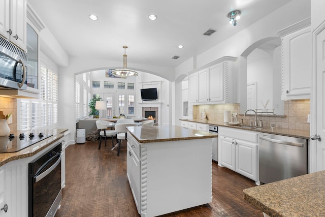 1891 Mustang Trl, Frisco, TX 75033 - kitchen with stainless steel appliances, a warm lit fireplace, tasteful backsplash, white cabinets, and a kitchen island