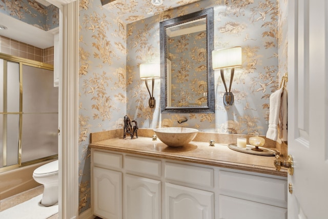 bathroom with wallpapered walls, vanity, toilet, and bath / shower combo with glass door
