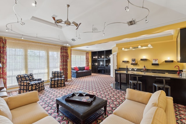 living area featuring a wealth of natural light, ornamental molding, a ceiling fan, and a raised ceiling