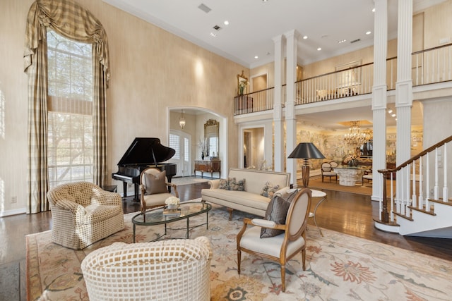 living room featuring crown molding, a notable chandelier, wood finished floors, and decorative columns