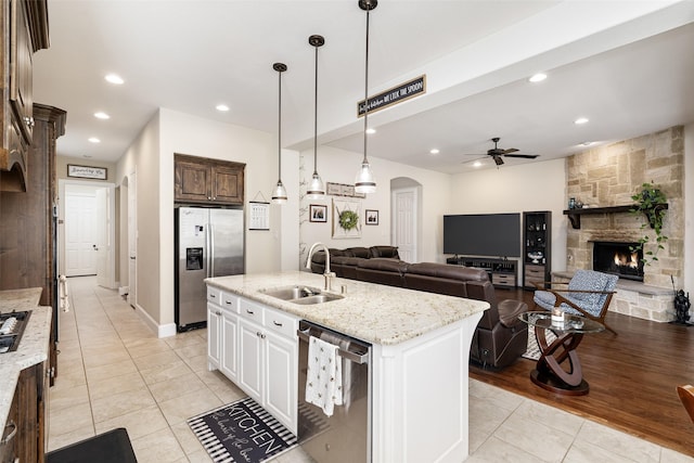 kitchen featuring stainless steel appliances, a sink, light tile patterned flooring, arched walkways, and a kitchen island with sink