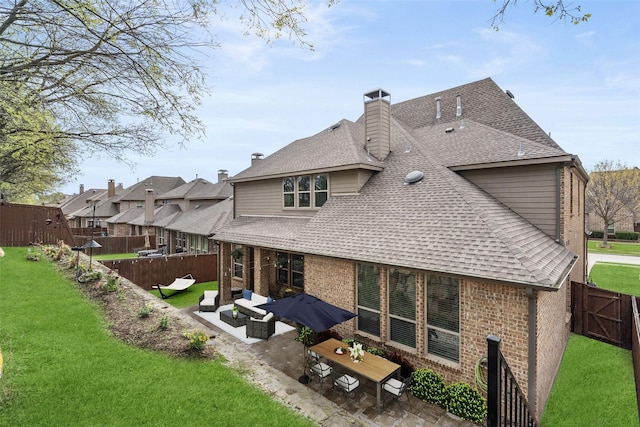 rear view of property with roof with shingles, a fenced backyard, brick siding, a patio area, and a yard