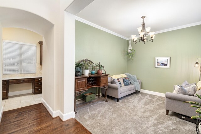 sitting room with an inviting chandelier, ornamental molding, arched walkways, light wood-type flooring, and baseboards