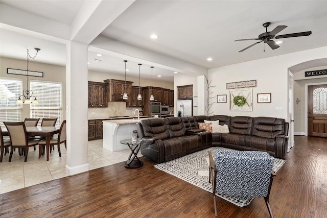 living area featuring arched walkways, plenty of natural light, light wood finished floors, and ceiling fan with notable chandelier