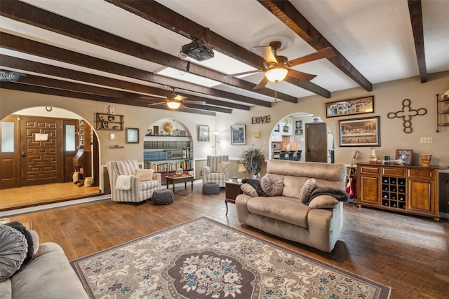 living area featuring beamed ceiling, wood finished floors, arched walkways, and a ceiling fan