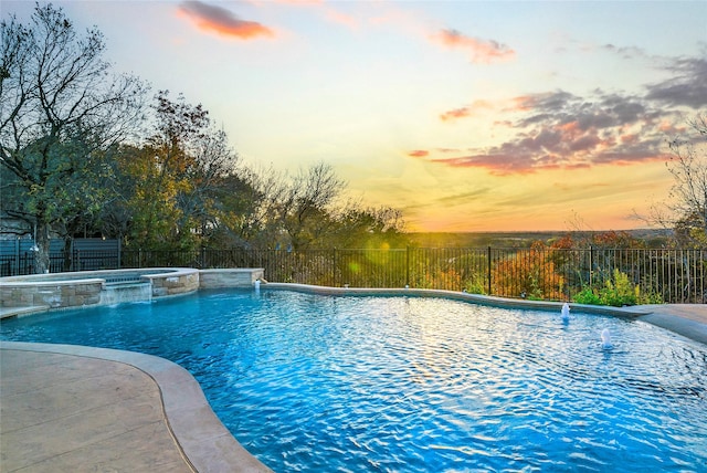 pool at dusk with fence and a pool with connected hot tub