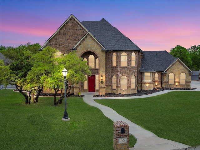 french country inspired facade with a lawn, a shingled roof, and brick siding