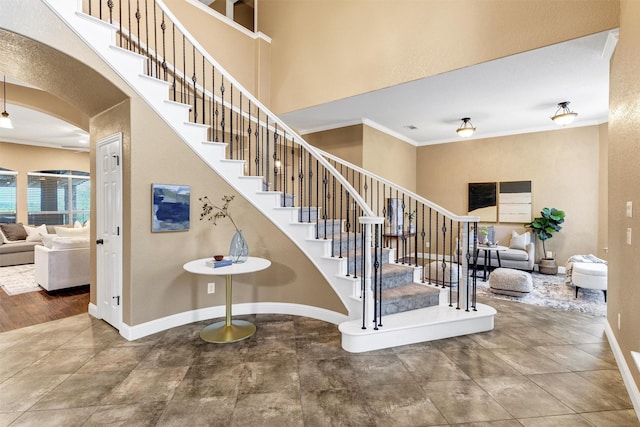 stairs with a towering ceiling, visible vents, ornamental molding, arched walkways, and baseboards