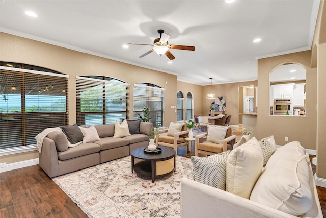 living room with arched walkways, baseboards, a ceiling fan, dark wood-type flooring, and ornamental molding